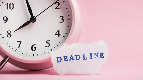 An alarm clock on a pink background beside a torn paper note reading DEADLINE