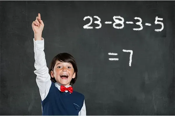 A boy excitedly raising his hand in front of a chalkboard that reads 23 − 8 − 3 − 5 = 7